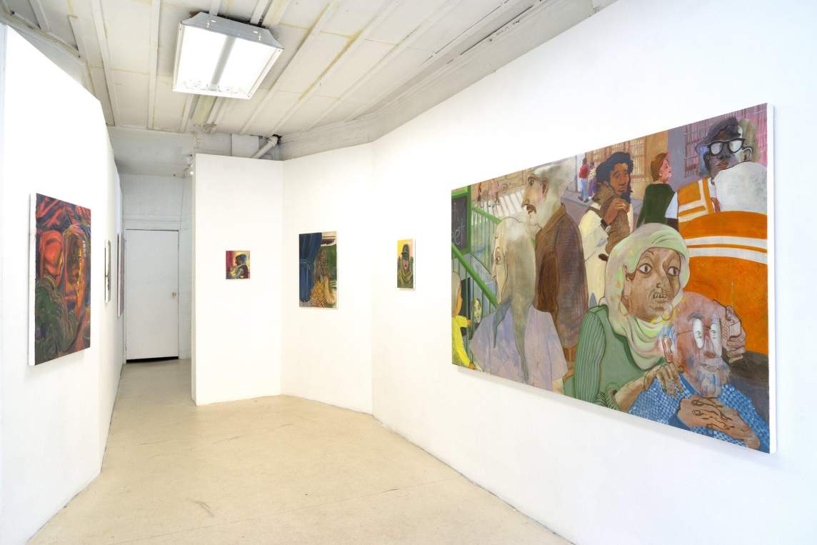 In a gallery space with white undulating walls and dark floor, paintings in various sizes hang on two facing walls. The largest painting shows a diverse group of people walking on a street in an urban environment.