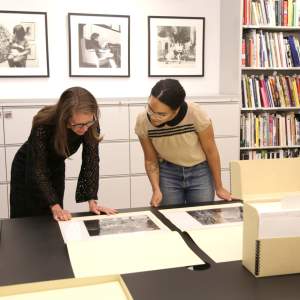 Two women lean over a table inspecting photographs in archive folders